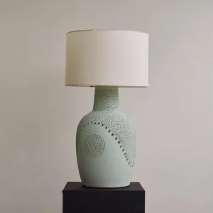 Matte sage green Jordyn table lamp with embossed dot pattern, unlit drum shade, studio display on black plinth