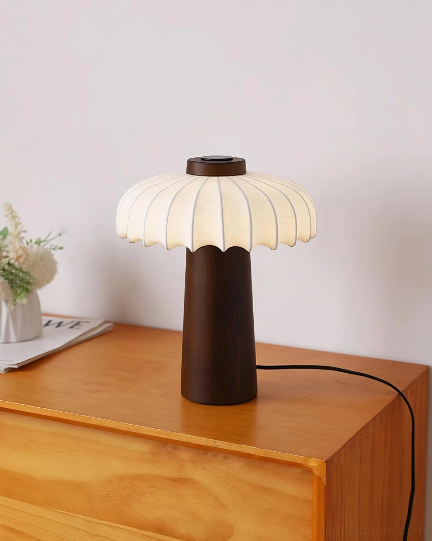 Lit Juego table lamp with dark wood base on wooden bedside dresser with glowing fabric shade