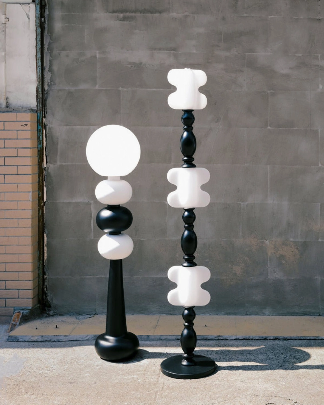 Two geometric modern floor lamps with stacked spheres against industrial brick wall outdoor setting