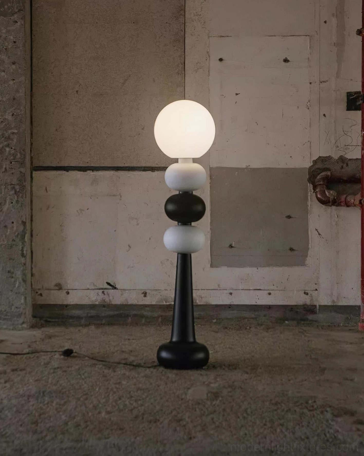 Illuminated Kabin floor lamp with geometric stacking glowing through frosted acrylic globe in concrete space with power cord