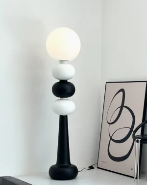 Black and white stacked sphere floor lamp in minimalist corner with abstract wall art decor, modern interior styling
