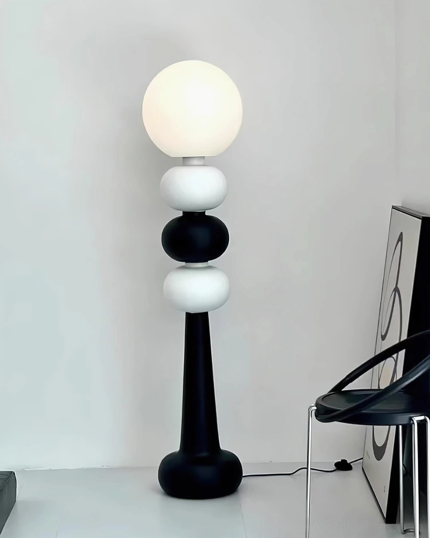 Contemporary floor lamp with stacked spheres in corner with black chair and modern art wall decor, minimal interior