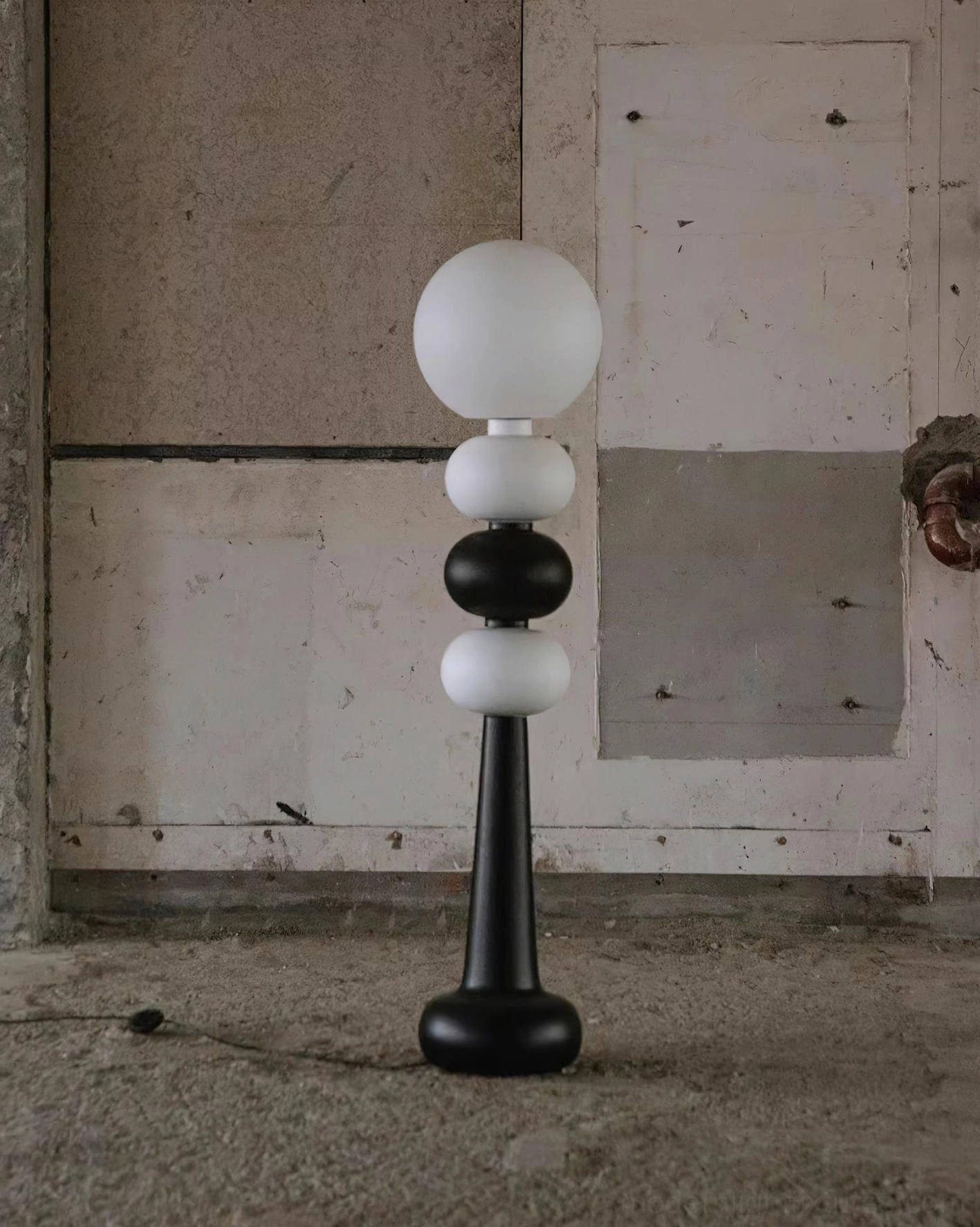 Unlit geometric floor lamp with frosted globe and matte black-white sphere finish against rough concrete wall