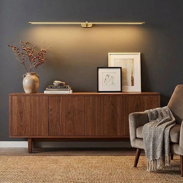 Kady Linear rechargeable wall sconce in minimalist living room setting, brass gold color above wooden console, warm ambient light