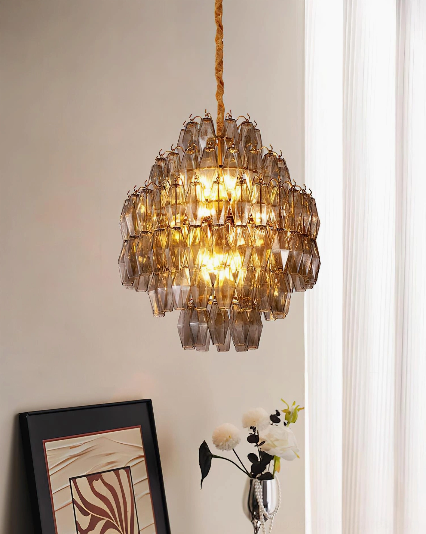 Contemporary tiered amber glass chandelier side hanging view in minimalist modern interior with wall art