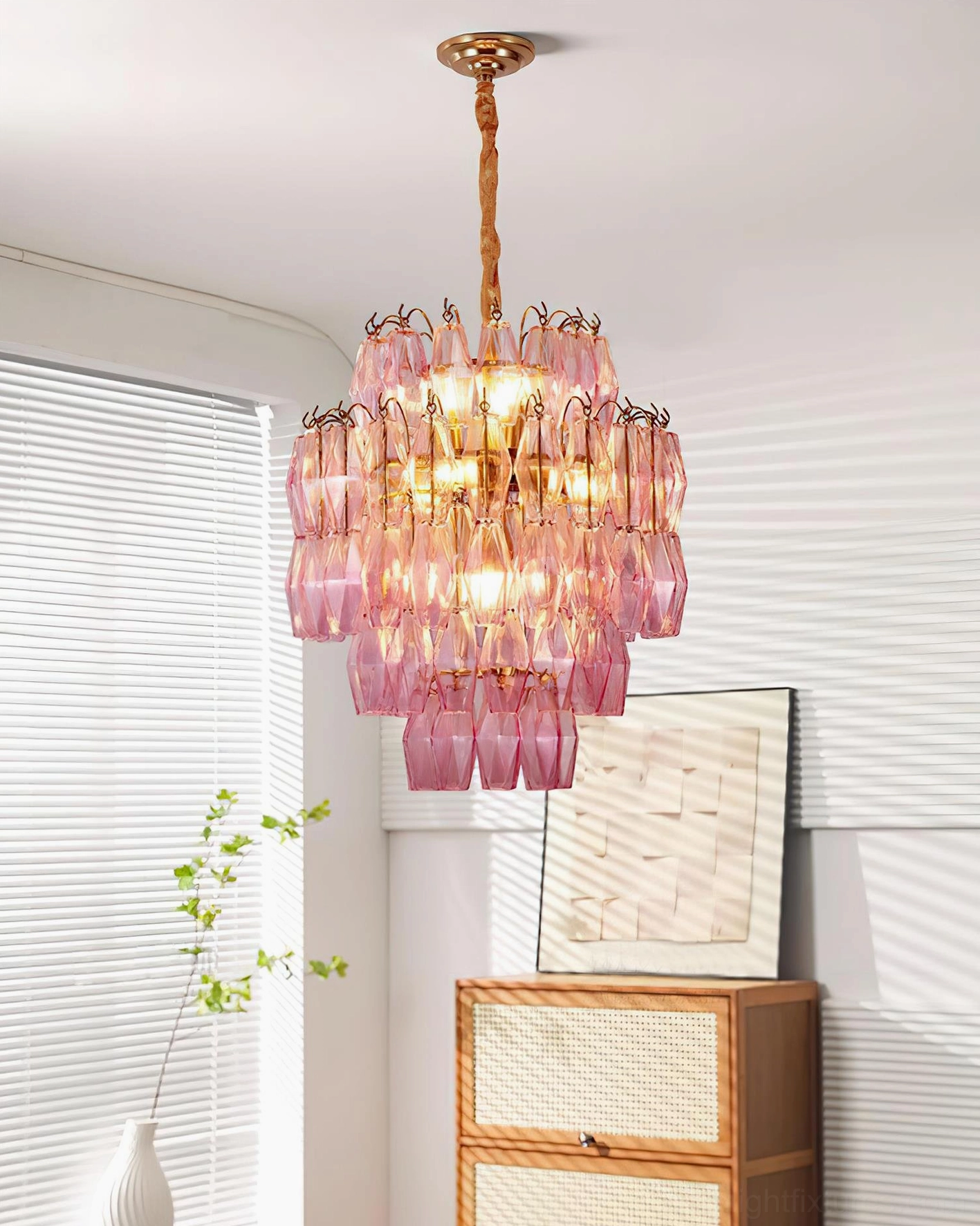 Modern tiered pink glass chandelier hanging in bright living room with window blinds, three-quarter suspended view