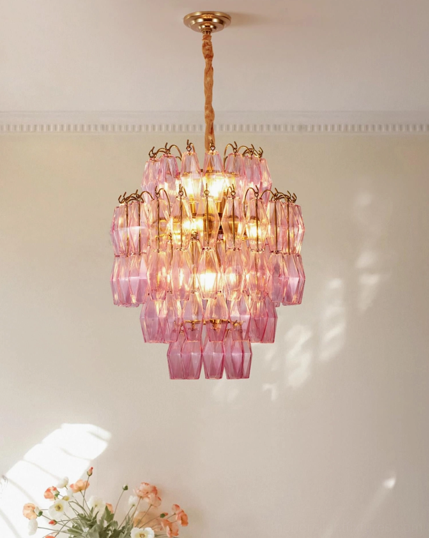Blush pink tiered glass chandelier with geometric facets, side hanging view in cozy interior with floral wall decor