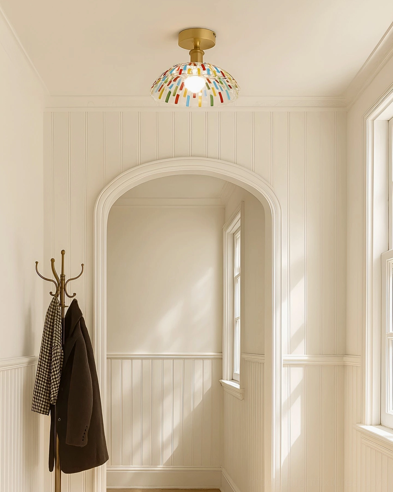 Kaleido glass ceiling light fixture installed in residential entryway with wainscoted walls, warm brass hardware, colorful stained glass shade