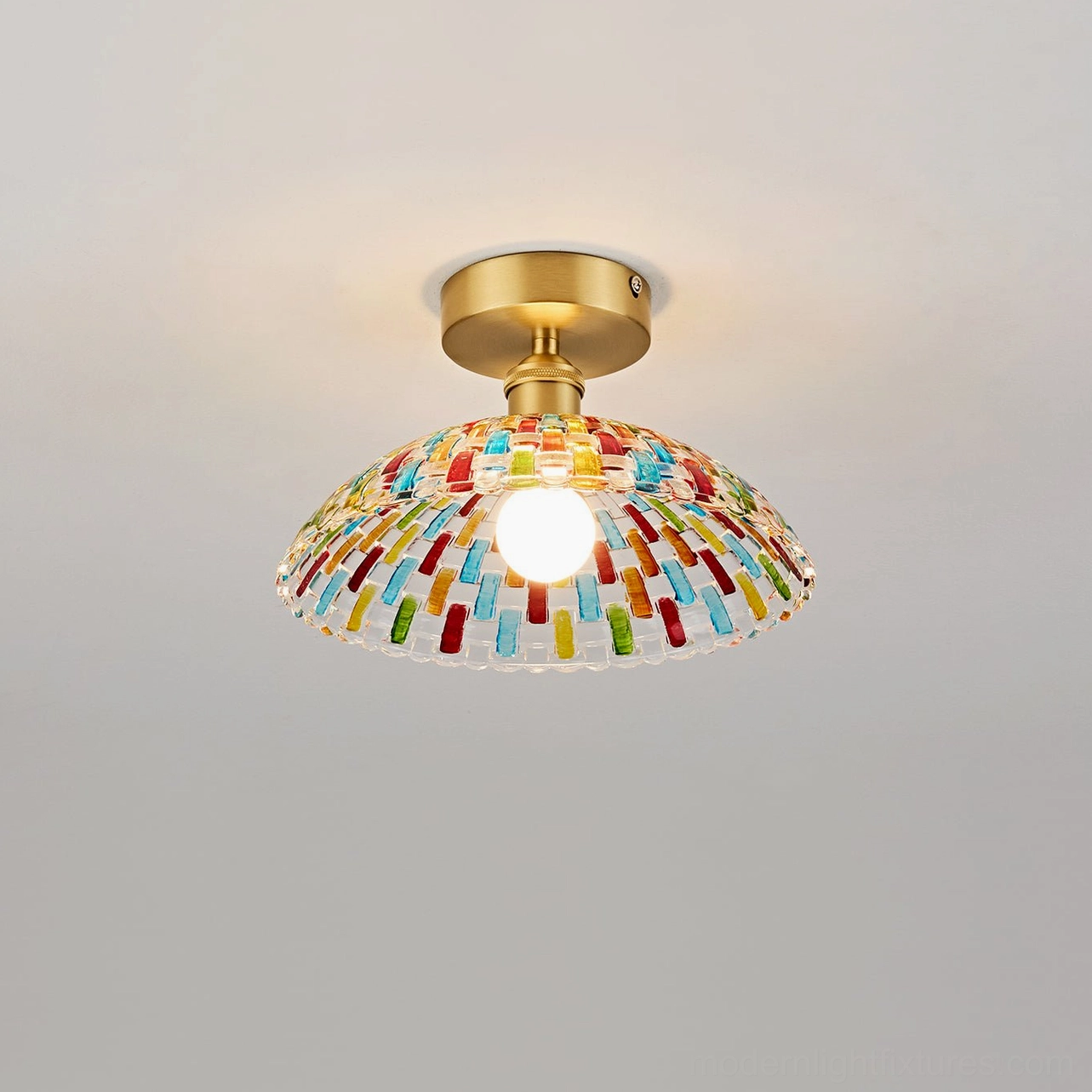 Kaleido glass ceiling light fixture low-angle front view with illuminated exposed bulb, colorful mosaic glass shade, brass hardware