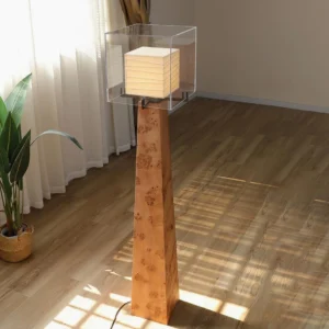 Kayne floor lamp low-angle side view in sunlit living room with natural light illuminating the tapered wood stand and glowing pleated paper shade interior
