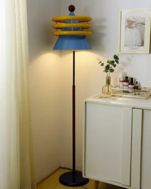Contemporary blue floor lamp with red top and yellow rings in residential corner, three-quarter angle view with warm lighting