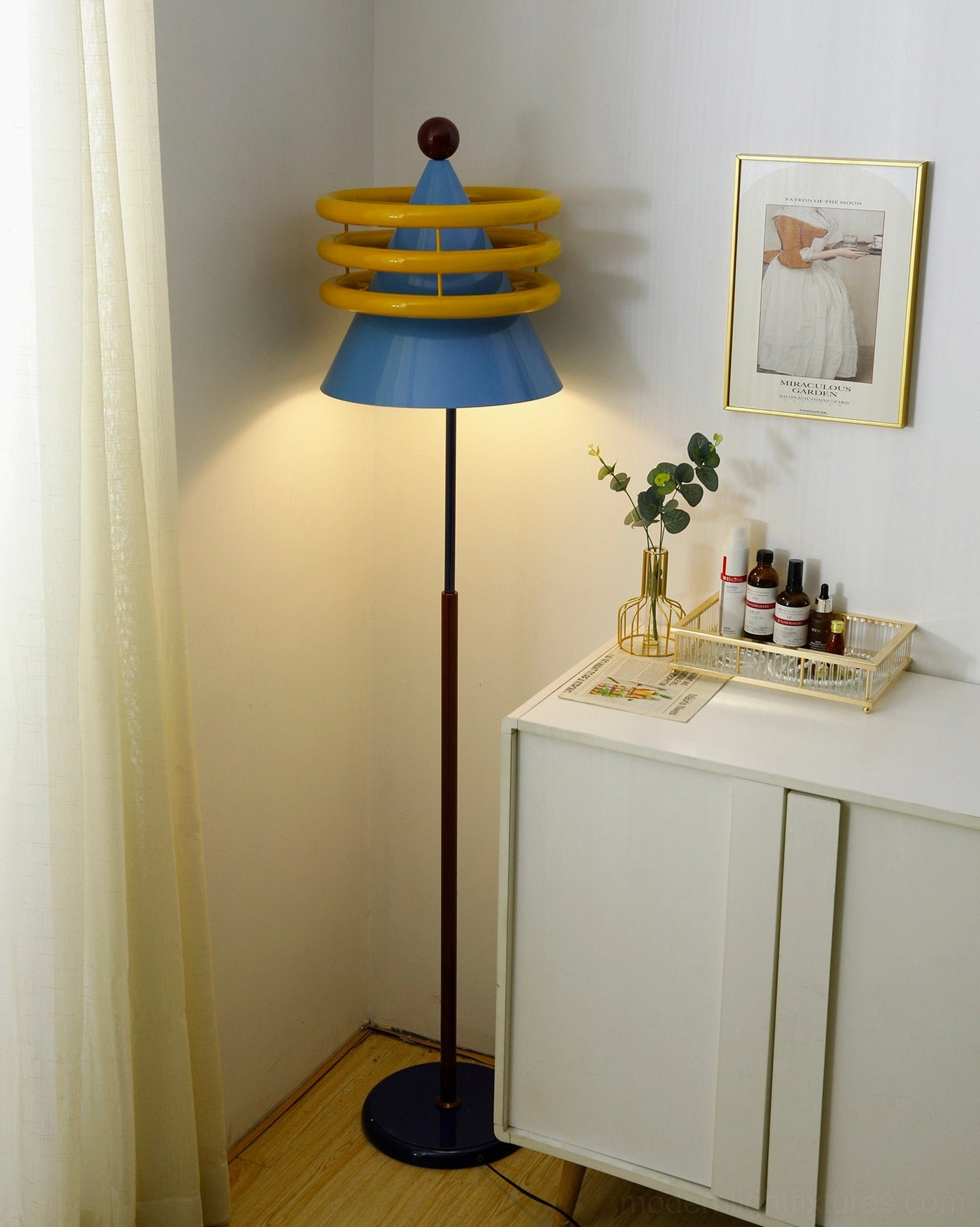 Modern geometric floor lamp beside green potted plant and home accessories, side three-quarter view