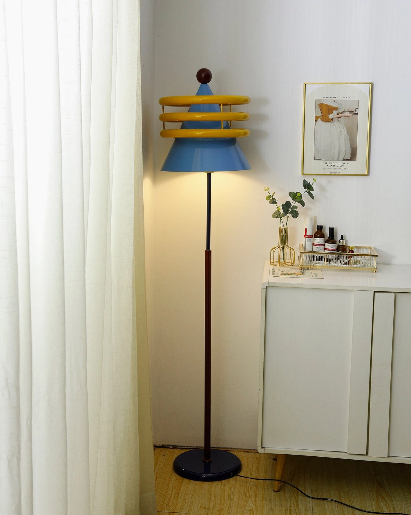 Blue and yellow modern floor lamp with extended power cord visible on residential floor, side angle view