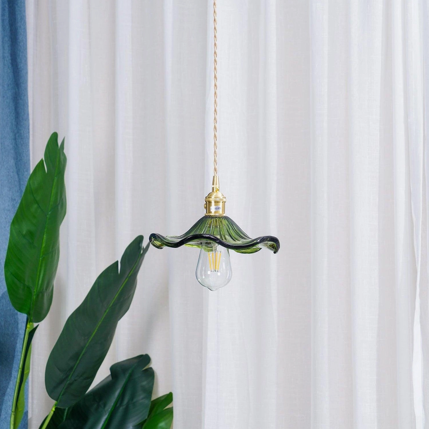 Single Kinney green ribbed glass pendant lamp hanging indoors with sheer white curtain and palm leaf decor