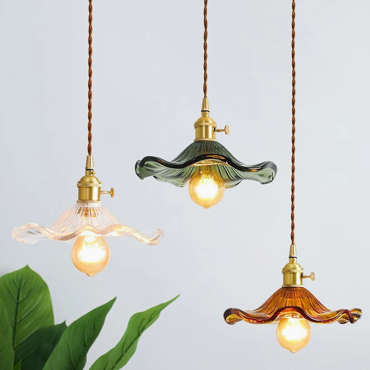 Three Kinney pendant lights in clear, amber, and green fluted glass hanging together with twisted cord over potted plant