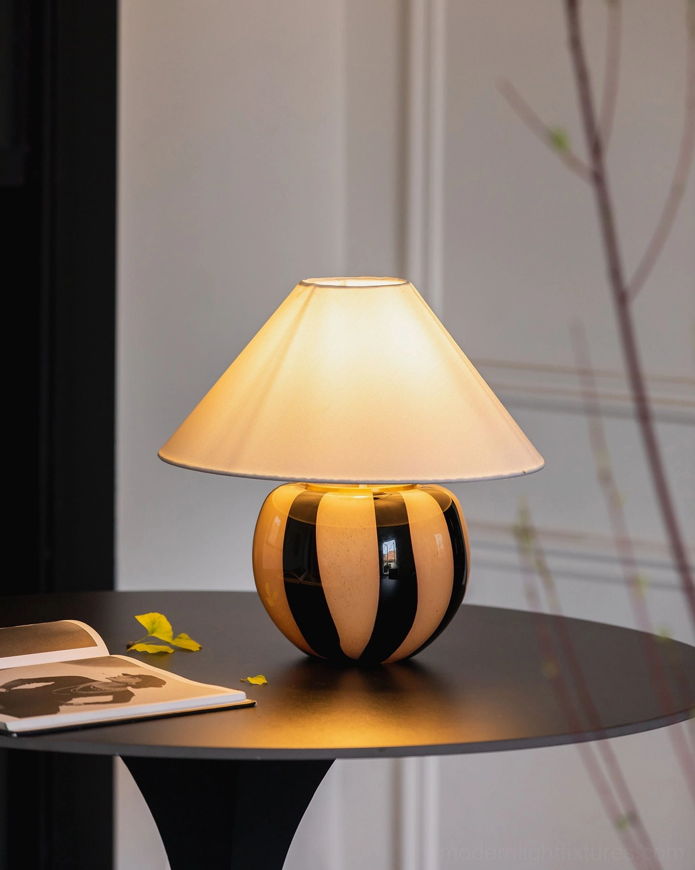 Kodhi striped ceramic table lamp with warm glow on black round side table, modern home styling