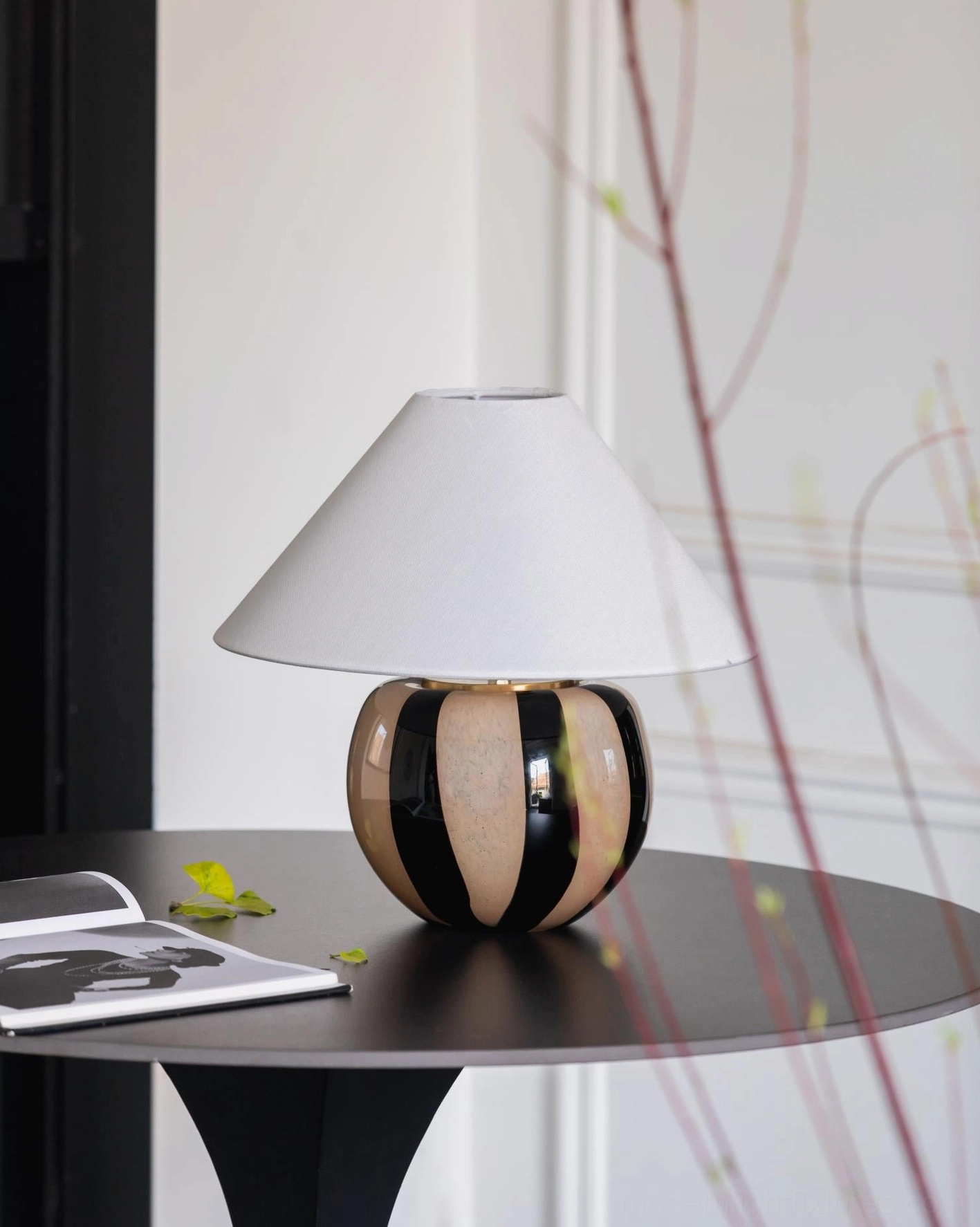 Kodhi table lamp three-quarter side view unlit on black side table with magazine and plant styling