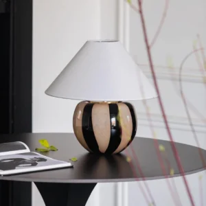 Kodhi table lamp with black and taupe ceramic base and white linen shade, three-quarter view on black side table