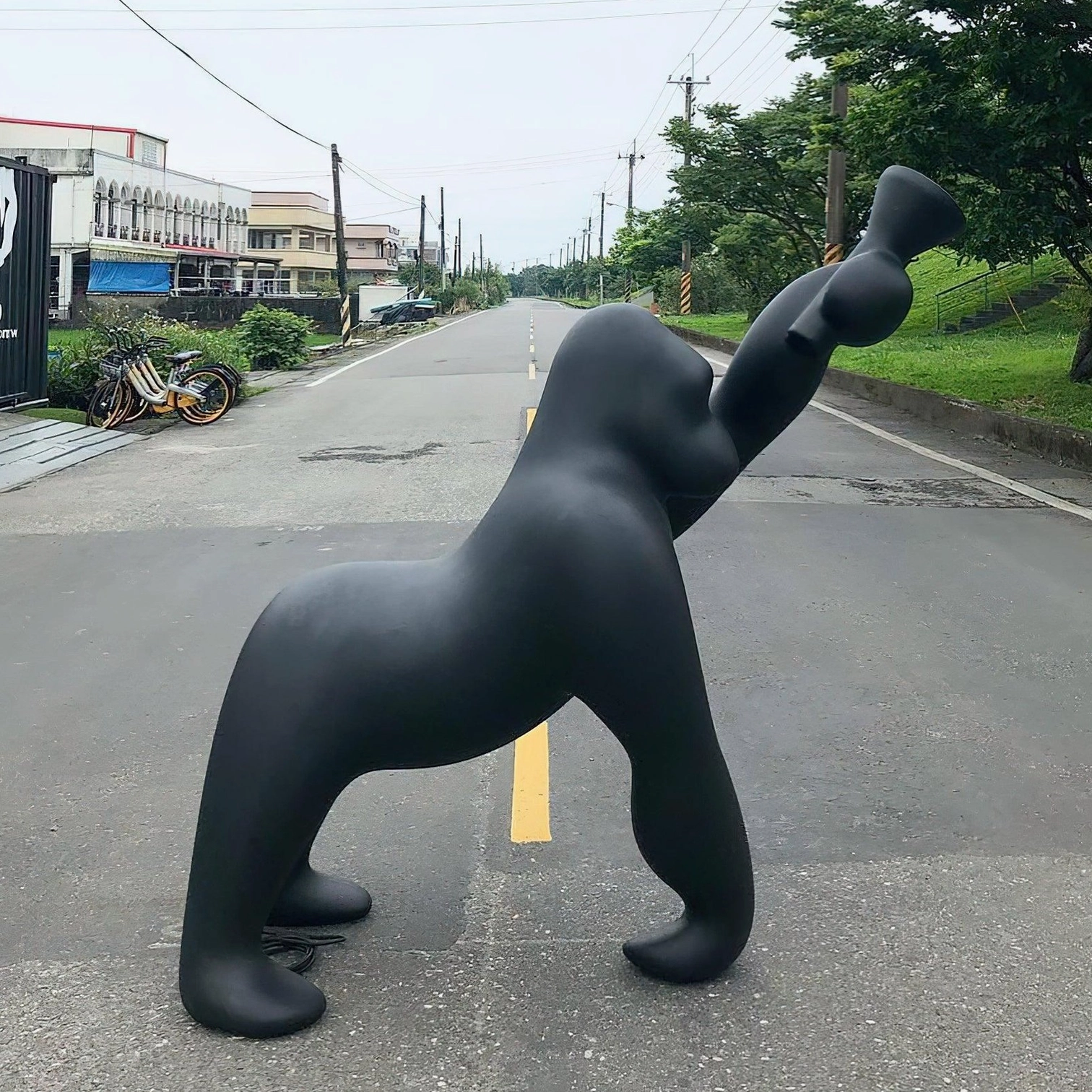 Kong sculptural floor lamp rear three-quarter view on urban residential street, emphasizing large-scale matte black artistic decorative lighting
