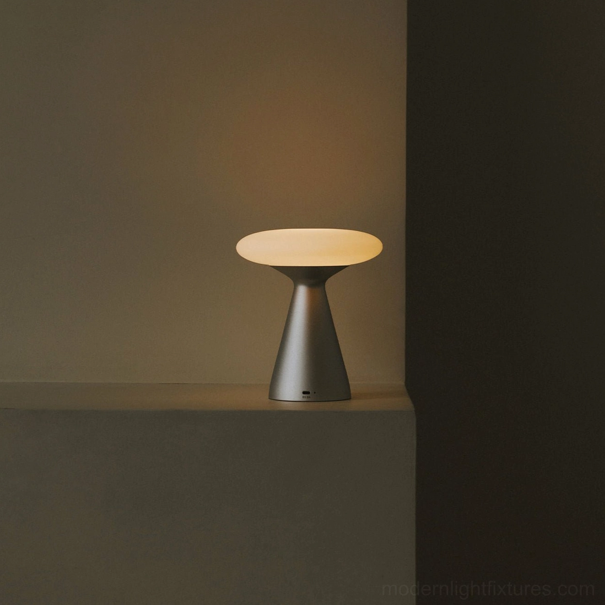 Konos table lamp emitting warm ambient light from low side angle on indoor wall ledge - compact minimalist lighting design