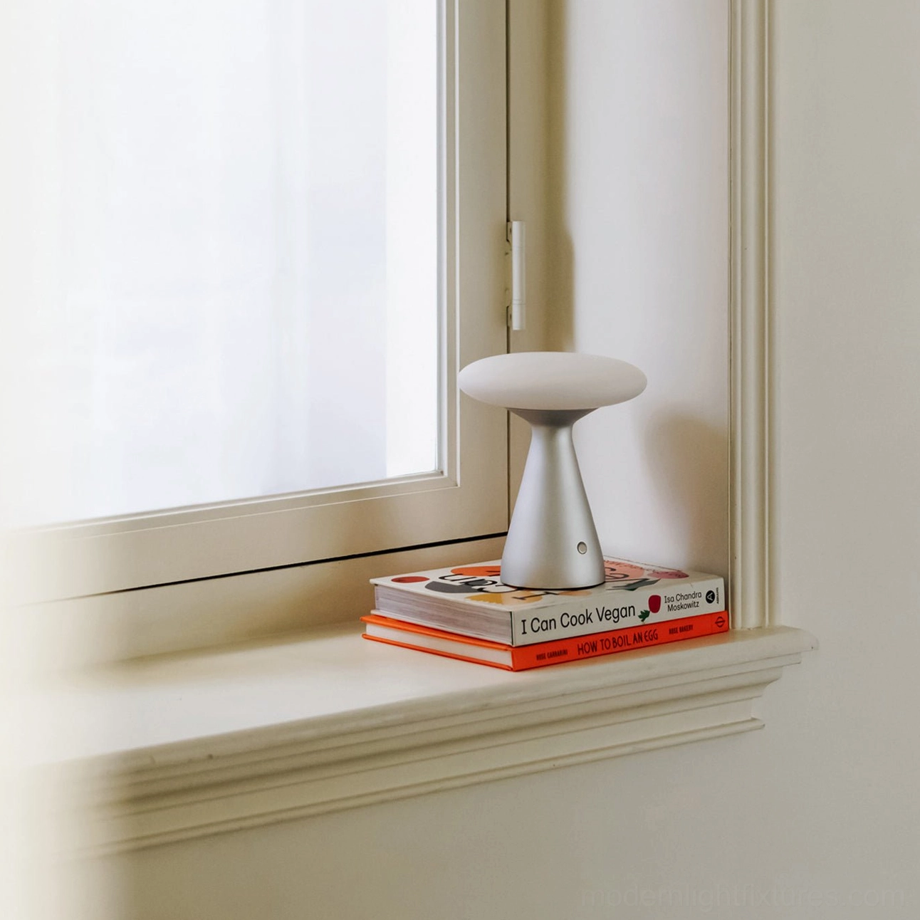 Konos modern table lamp on residential windowsill stacked on vegan recipe cookbooks - Scandinavian minimalist home interior