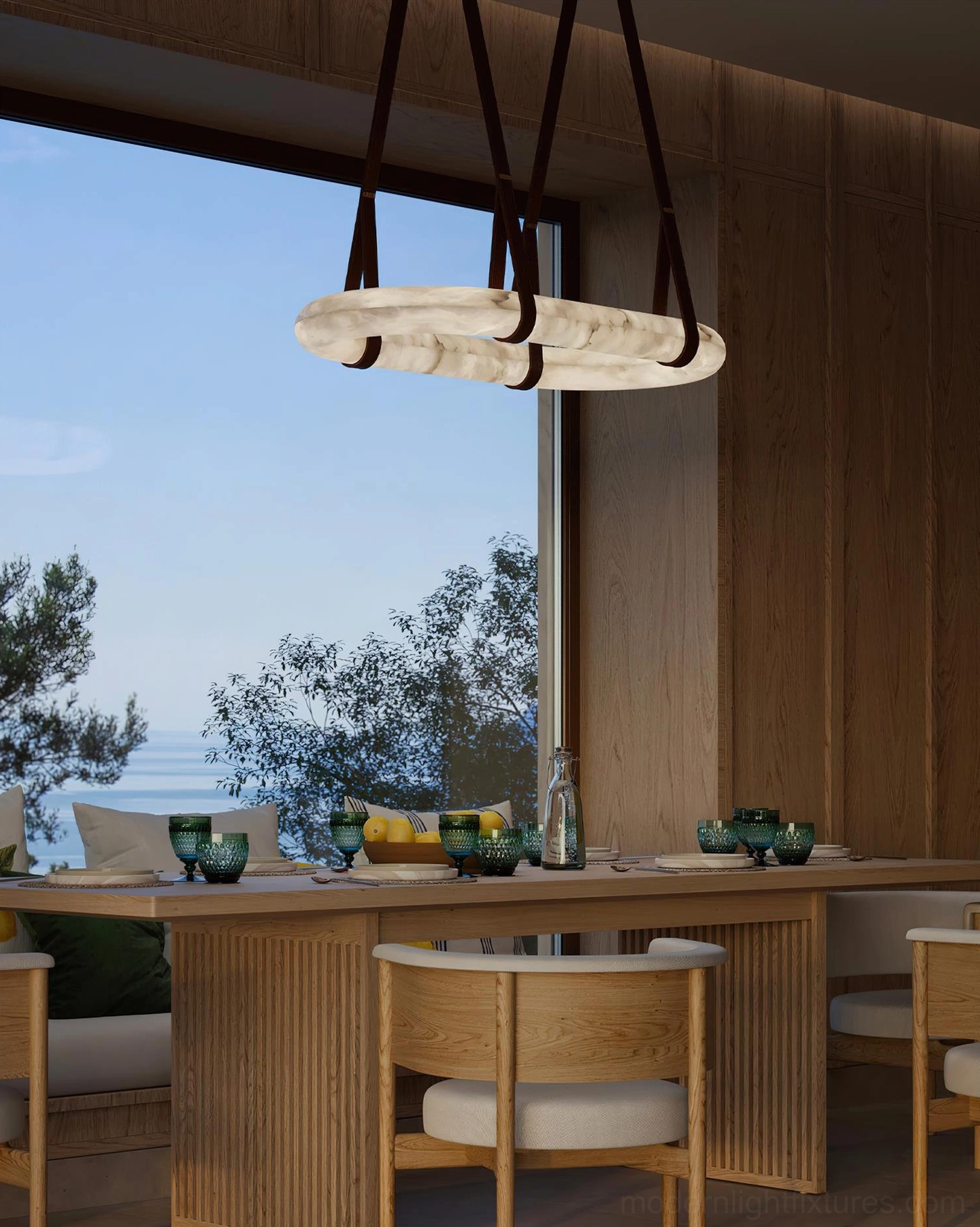 Small oval alabaster pendant chandelier hanging over long dining table in coastal residential dining space with natural light