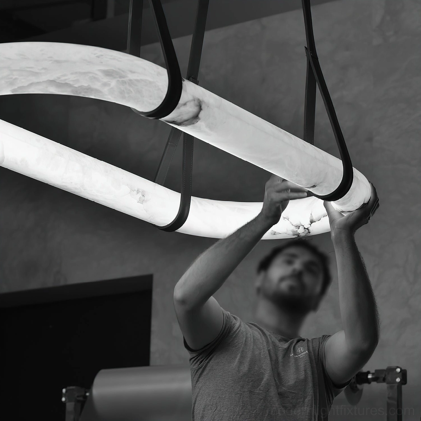 Close-up eye-level view of Kurve alabaster ring lighting fixture with black metal fasteners and hardware in workshop setting