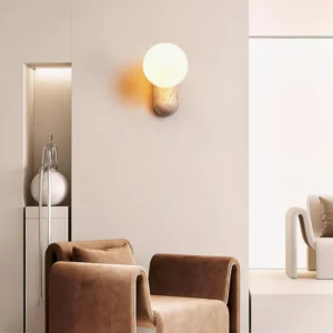 Kyomi wall sconce three-quarter angle installed in residential hallway niche, warm earthen stone base with glowing white shade