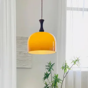 Warm amber glass pendant light hanging in bright interior with green plants and sheer curtains - mid-century modern home lighting