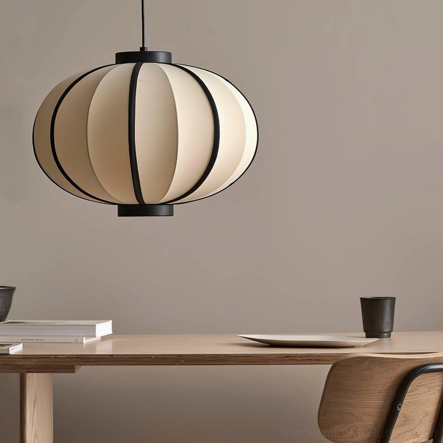 Modern lantern pendant light suspended above wooden dining table with tableware setting