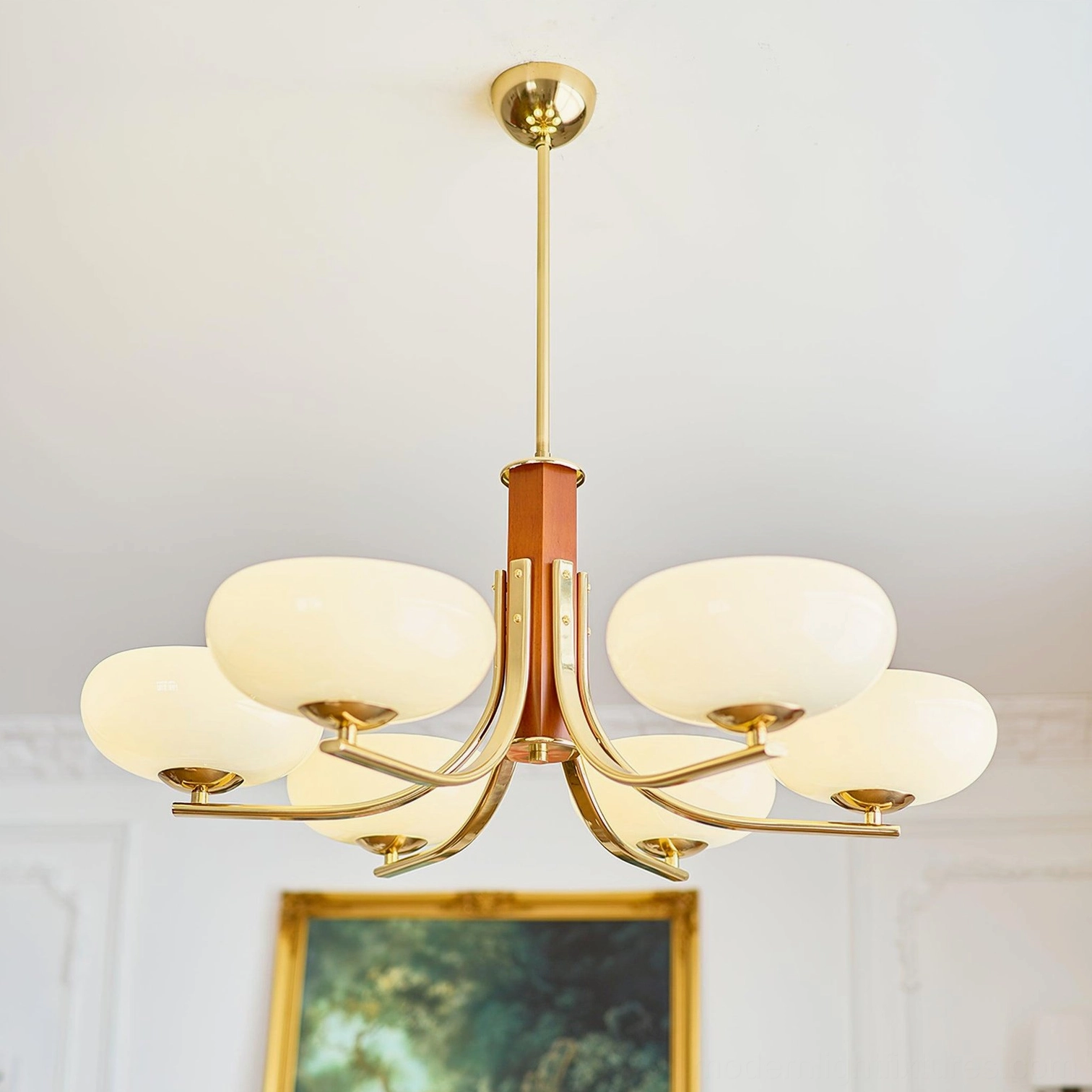 Retro pendant chandelier with gold metal arms, brown solid wood central stem, and milky glass lamp covers in decorated living room setting