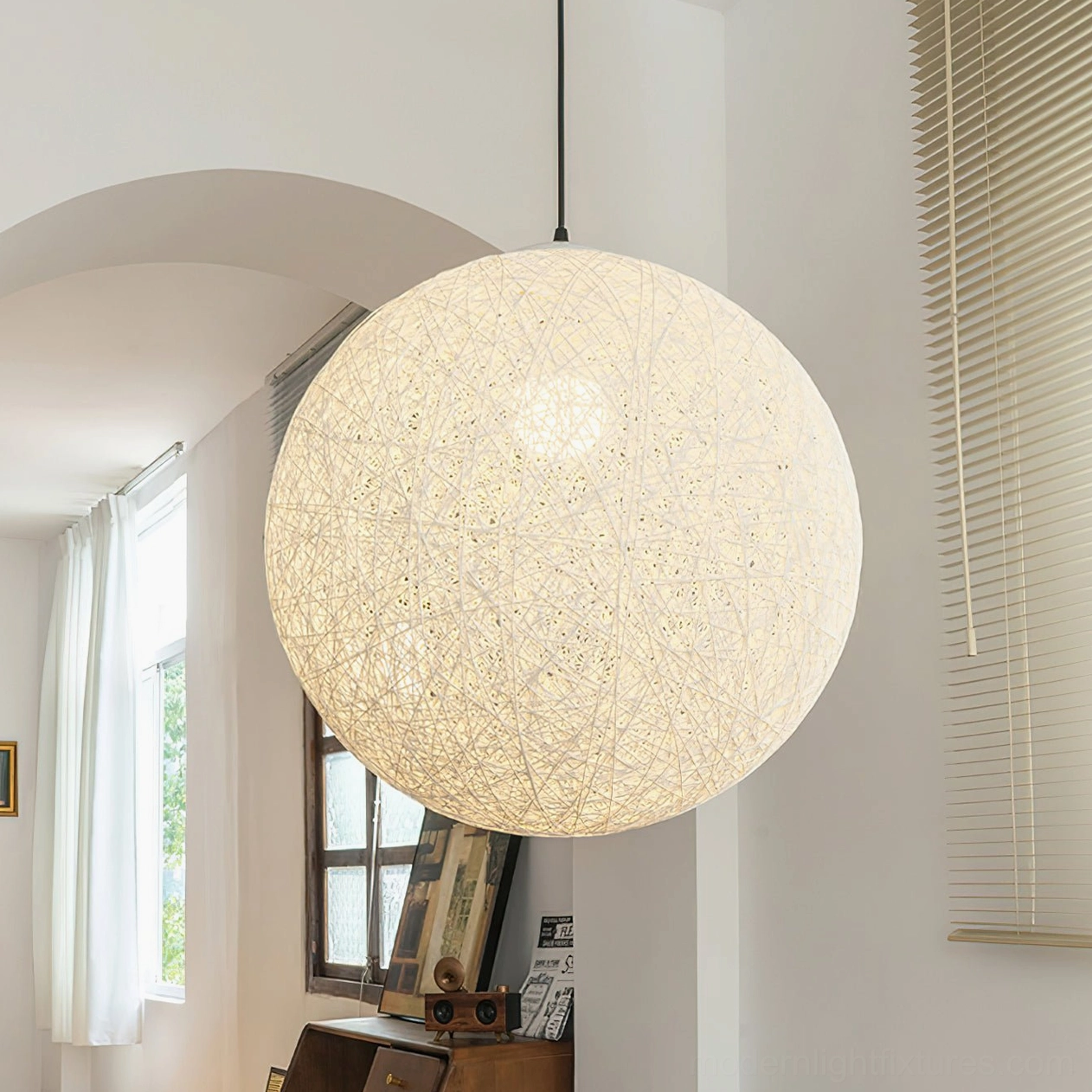 Large handwoven hemp sphere pendant light side profile view in residential space with arched doorway, bright natural illumination