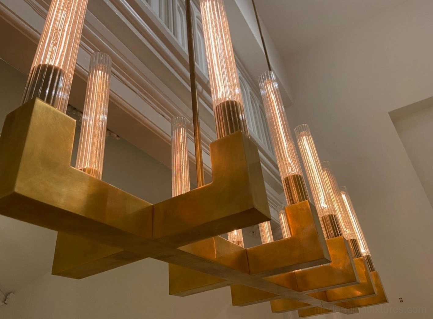 Large linear brass chandelier polished finish high-ceiling dining room warm glow lighting
