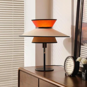 Mid-century modern layered table lamp with warm glowing fabric shade and pull-chain detail on bedroom side cabinet, contemporary interior design styling