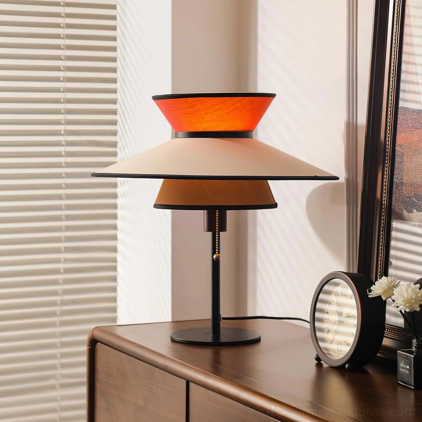 Mid-century modern layered table lamp with warm glowing fabric shade and pull-chain detail on bedroom side cabinet, contemporary interior design styling