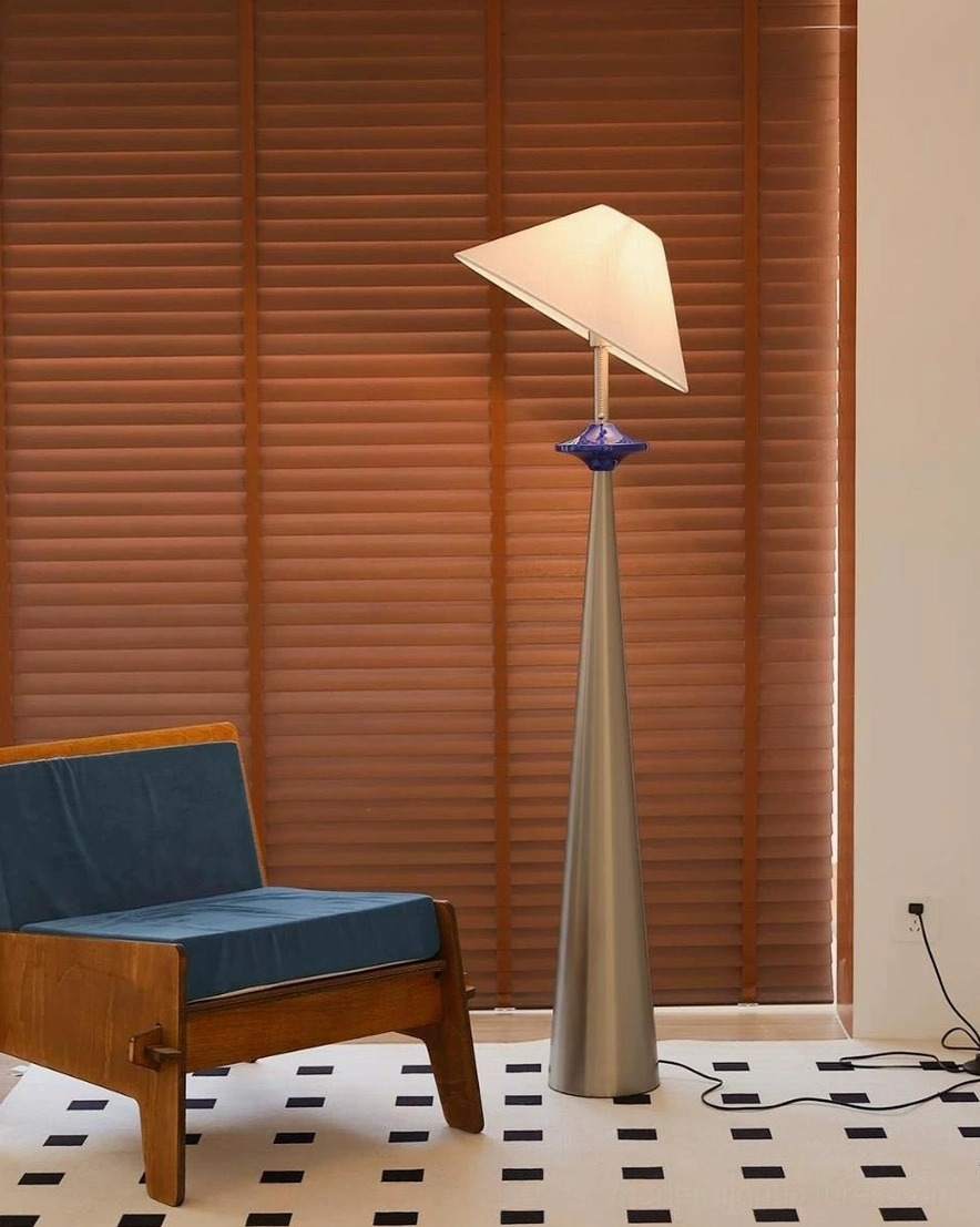 Asymmetrical cone floor lamp with off-white linen shade and silvered tapered pole in room with wooden window blinds