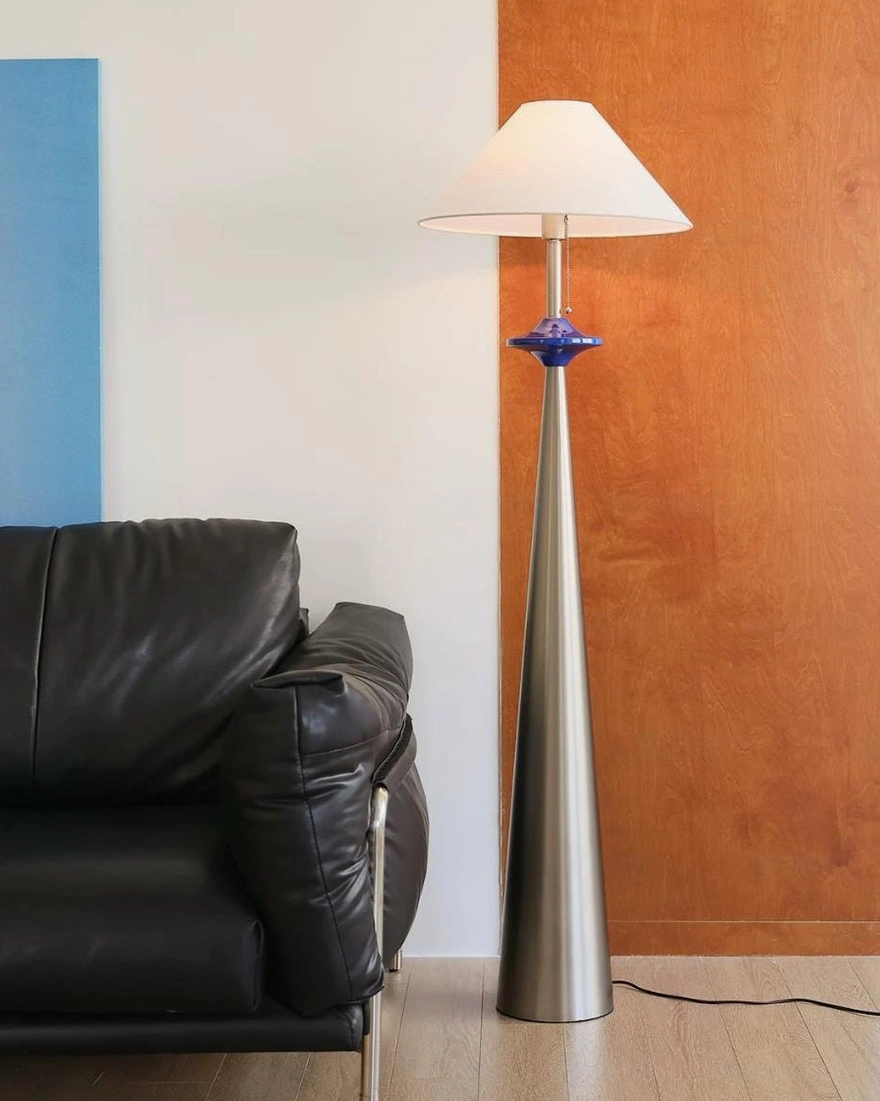 Mid-century modern cone floor lamp in living area with leather sofa, showcasing silver metal pole and white conical shade