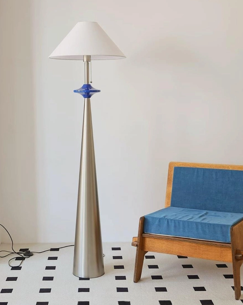 Cone floor lamp in minimalist interior with checkered tile flooring, side profile showcasing tapered stainless steel pole and fabric shade