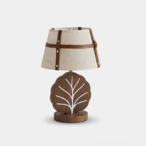 Leafora accent table lamp front view - ash wood leaf-shaped base with white vein inlay, tapered linen drum shade wrapped in saddle-brown leather straps with brass rivets