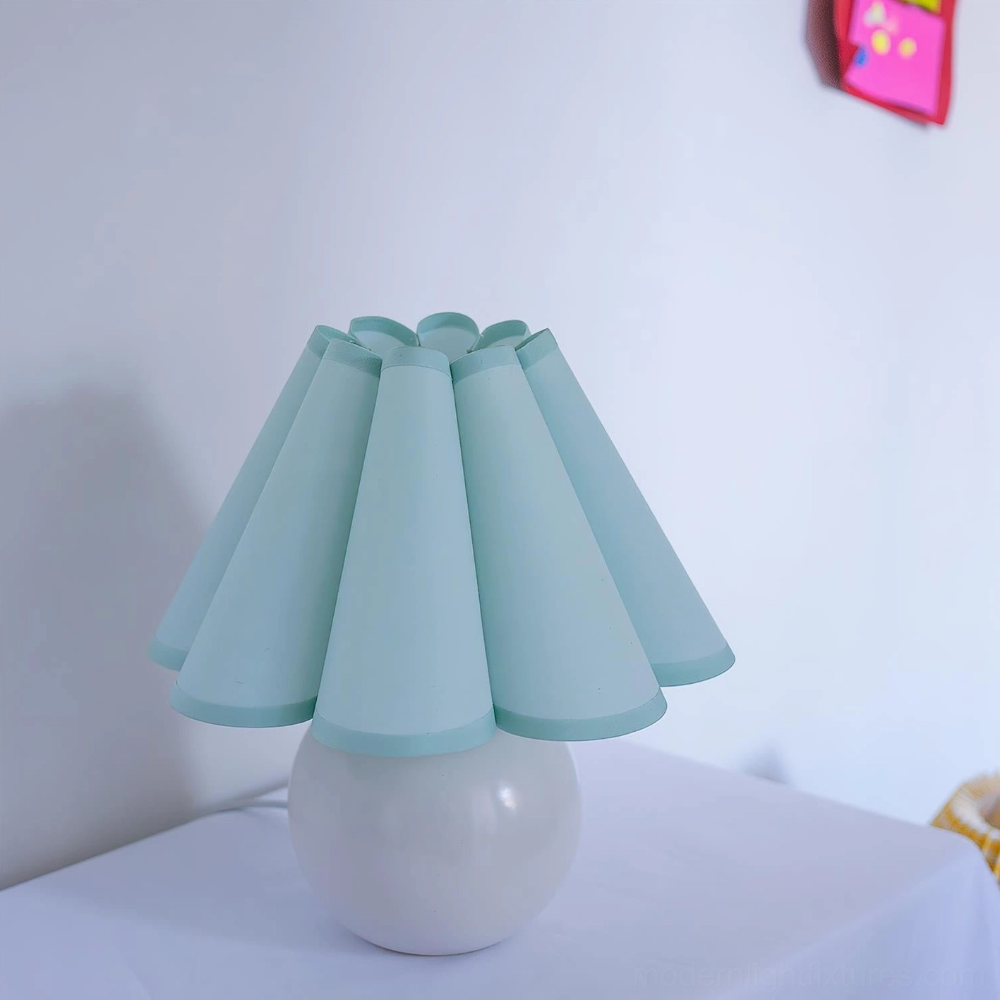 Modern pleated table lamp with white ceramic base and light blue pastel shade on minimalist indoor desktop