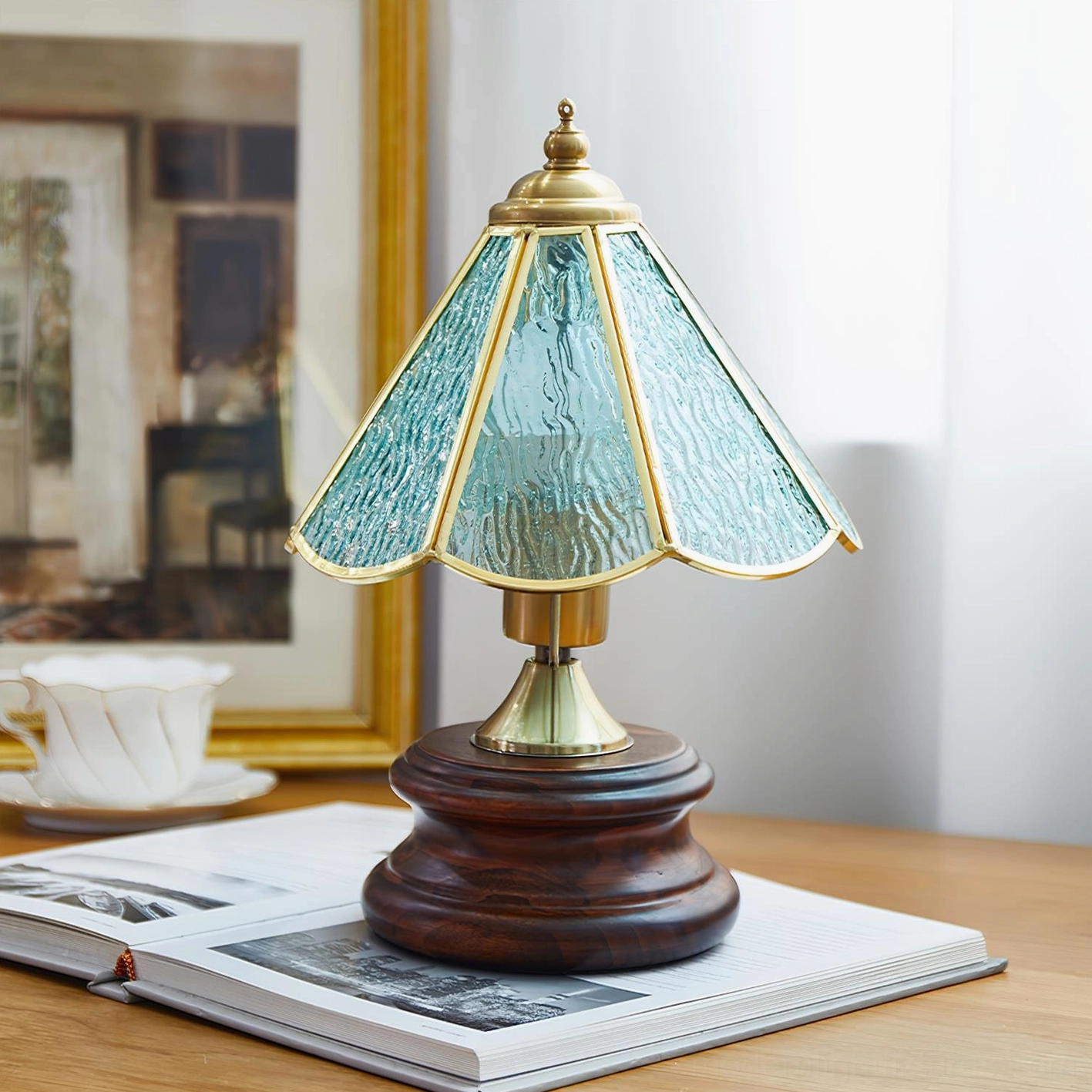Light blue stained glass table lamp with rippled glass panels and brass fixture on wooden desk with book and teacup styling