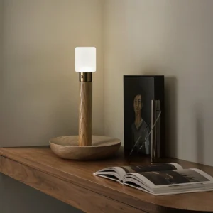 Light wood finish portable table lamp displayed on wooden console with home decor accessories in wabi-sabi style interior