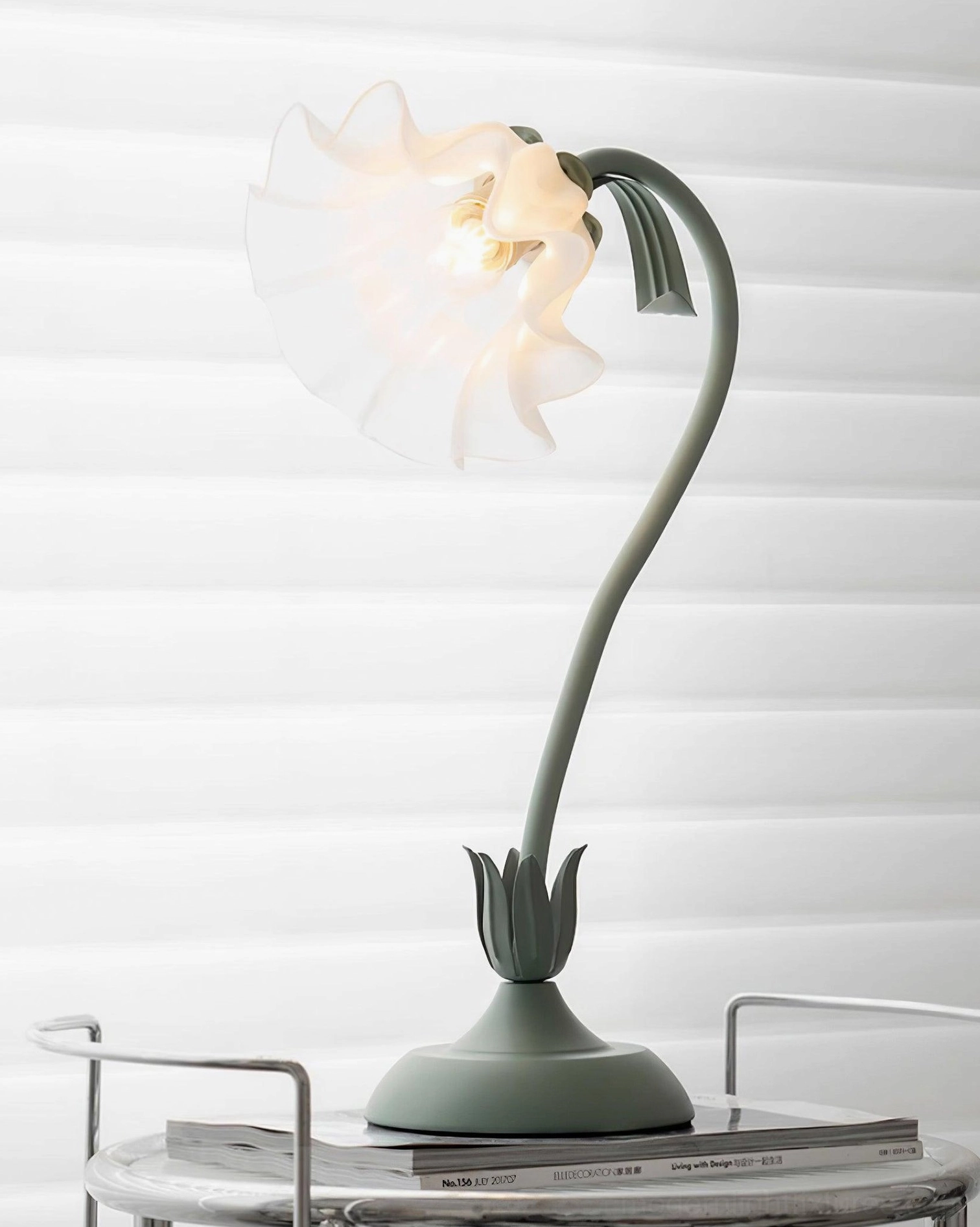 Modern lily flower table lamp illuminated on side table with louvered window backdrop showing curved green arm