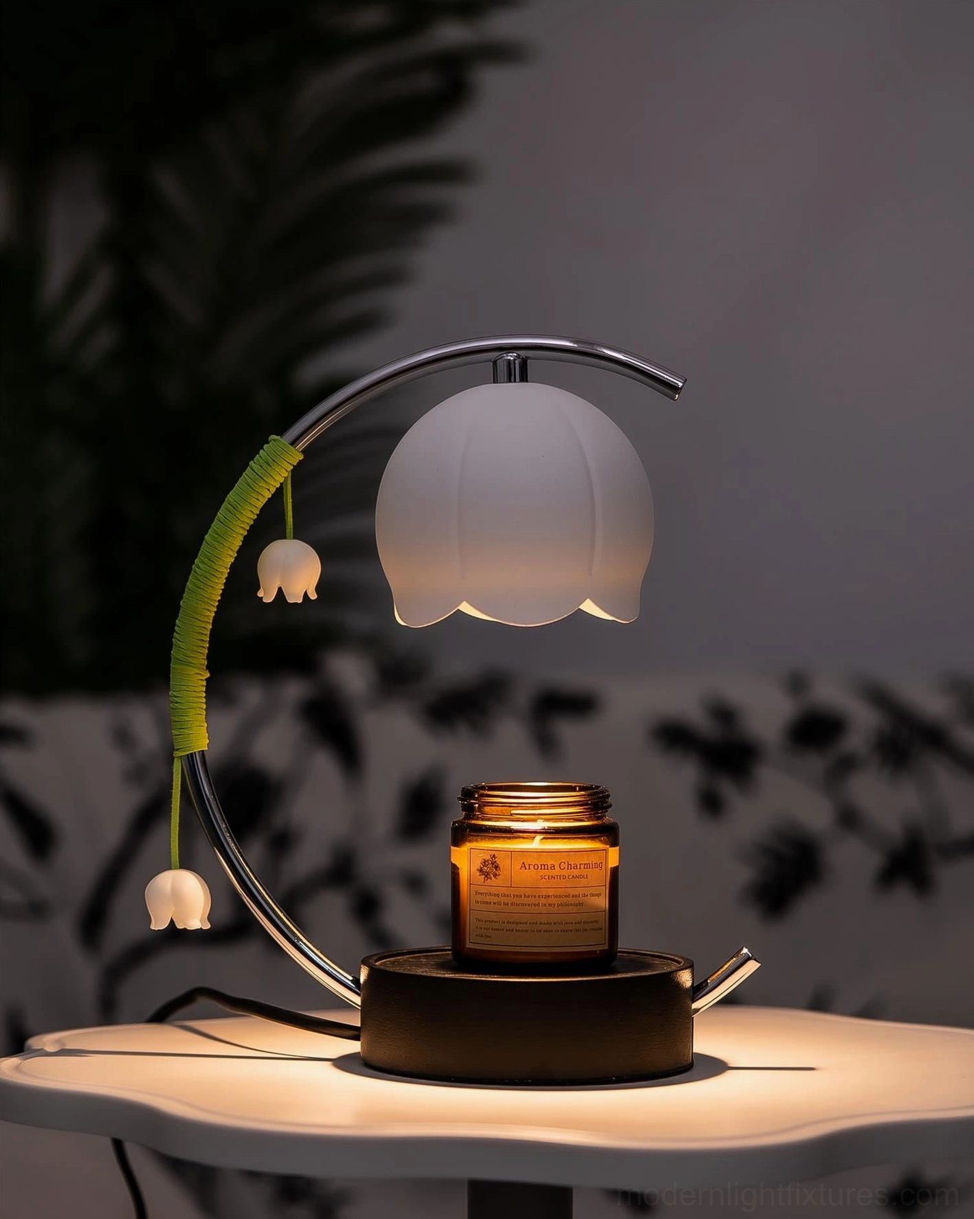 Modern botanical table lamp with white bell-shaped shade and lit scented candle jar with focused warm spotlighting