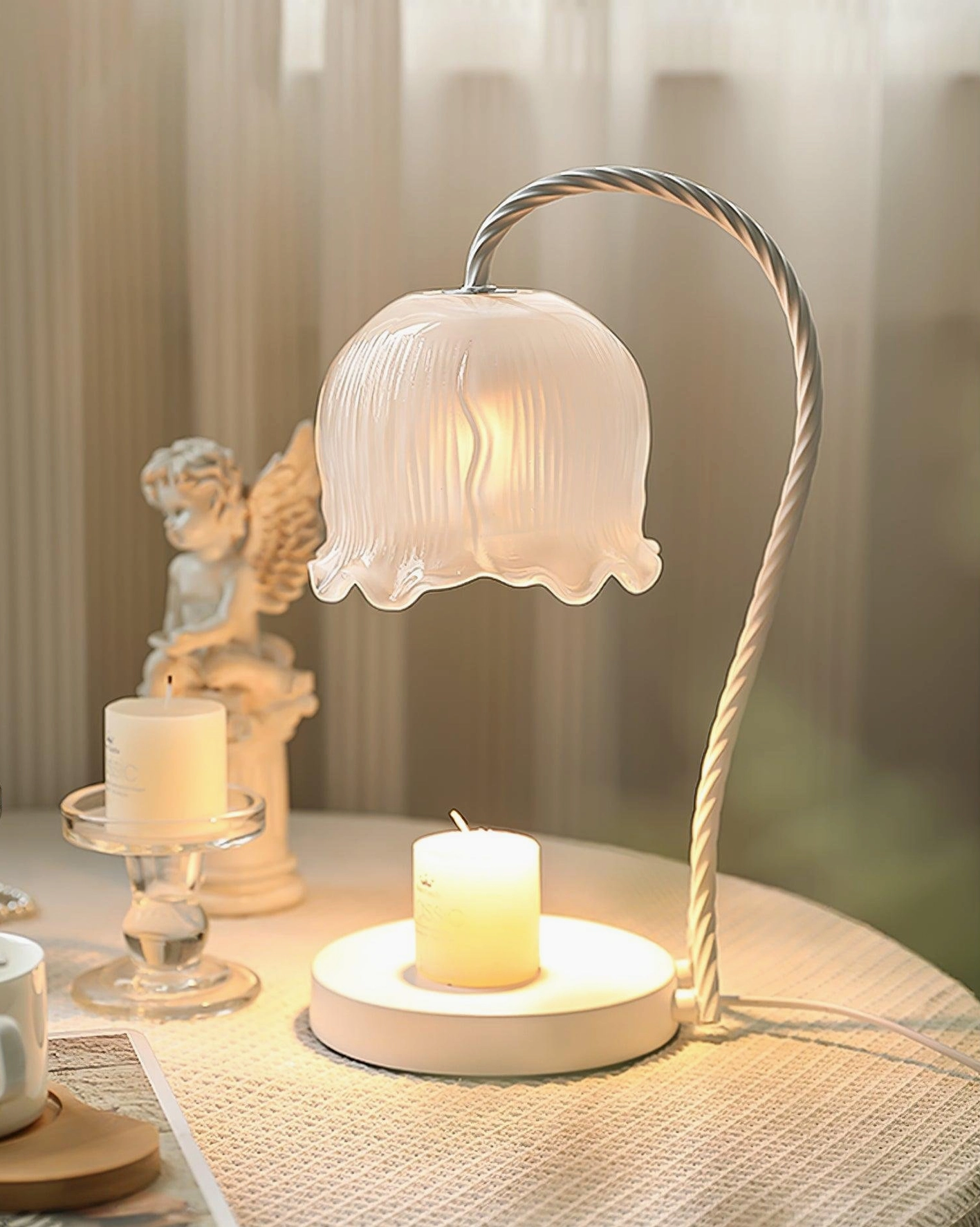 Lily of the valley candle warmer lamp styled with angel ornament and white scented candles on fabric tabletop