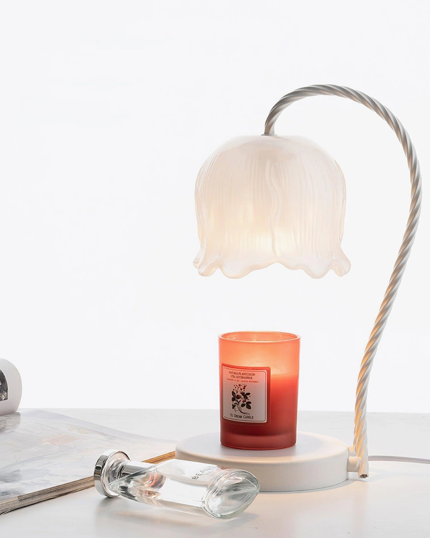 Lily of the valley candle warmer lamp on minimalist white desk with glass bottle and reading magazines