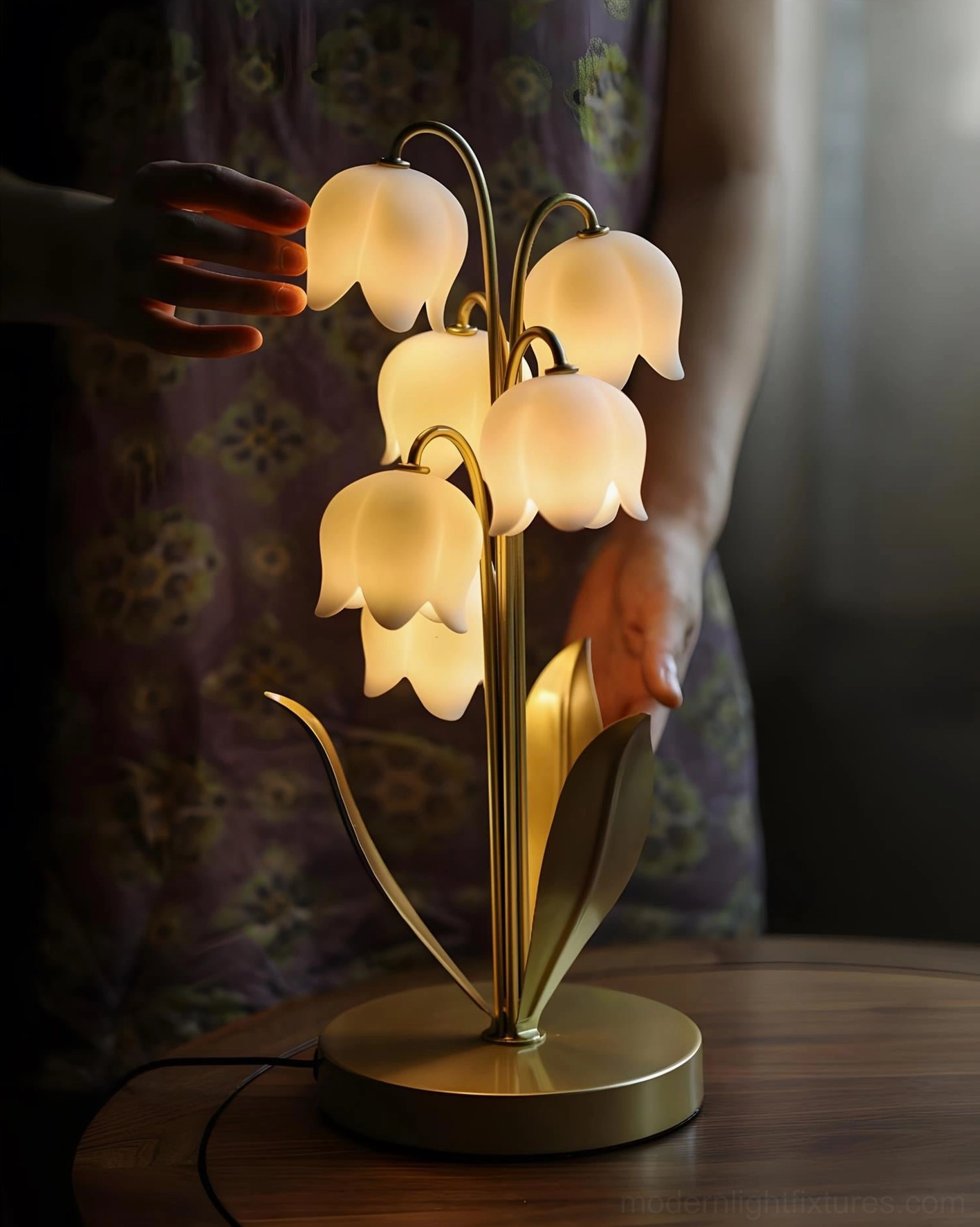 Close-up interactive view of lily of the valley table lamp showing gold metal base and curved stems with hands adjusting the sculptural design