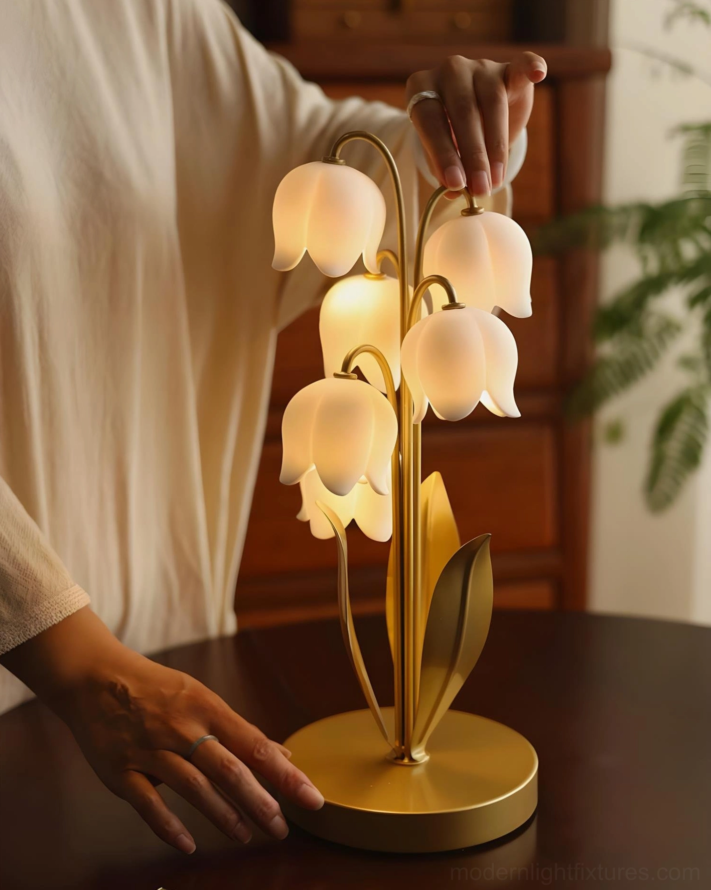 Contemporary lily of the valley table lamp with gold brass metal frame and curved sculptural stems, close-up detail on wooden desk