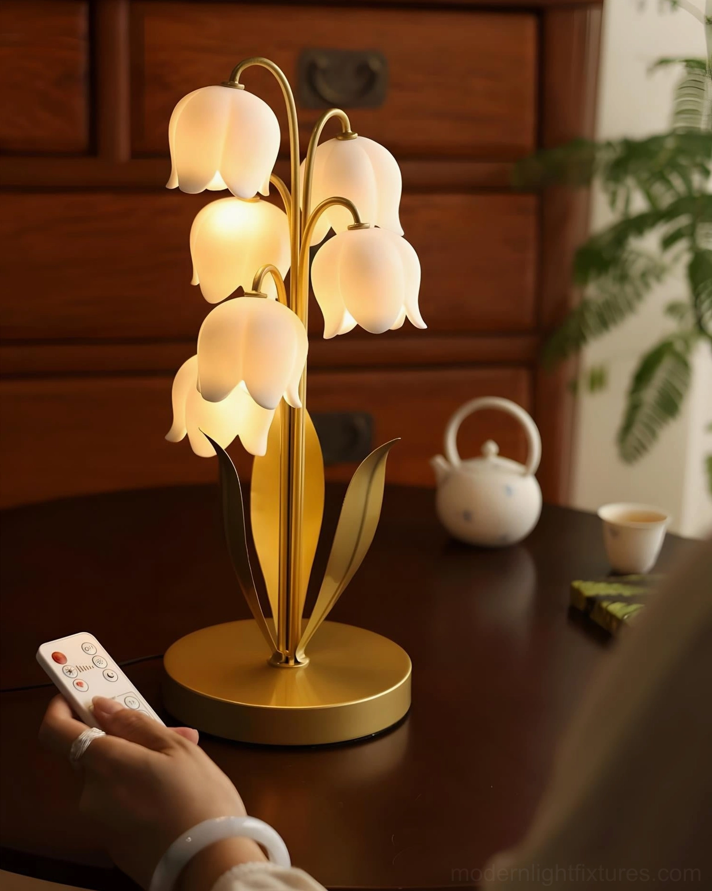 Botanical table lamp with gold metal frame and white frosted petal shades on wooden side table with tea set styling and warm ambient light