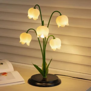 Modern lily of the valley desk lamp with warm glowing light on wooden desktop by window